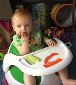 baby eating chicken drumstick, cucumber and red pepper