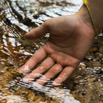white skinned hand dipped into a shallow stream of water